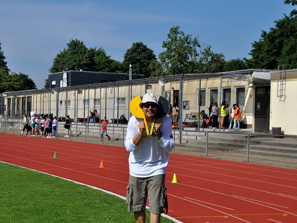 Person mit Kelle und Sonnenhut am Rand der Bahn.